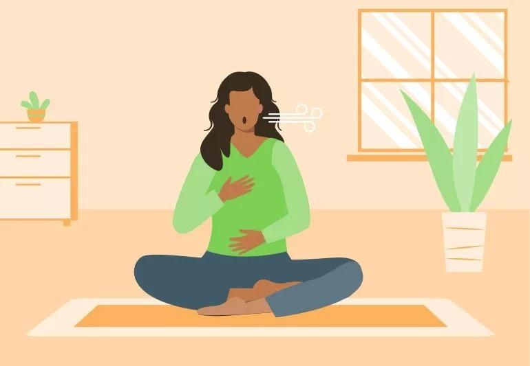 Kvinna sitter i skräddarställning och andas lugnt på en yogamatta