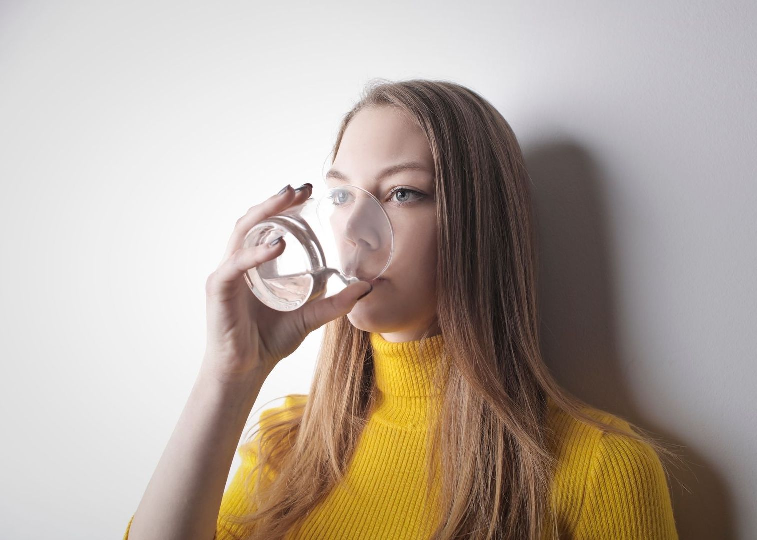 Kvinna i gul tröja dricker vatten ur ett glas i dagsljus
