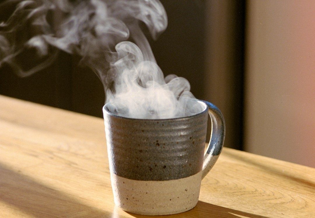 Ångande kaffekopp på ett träbord i morgonljus