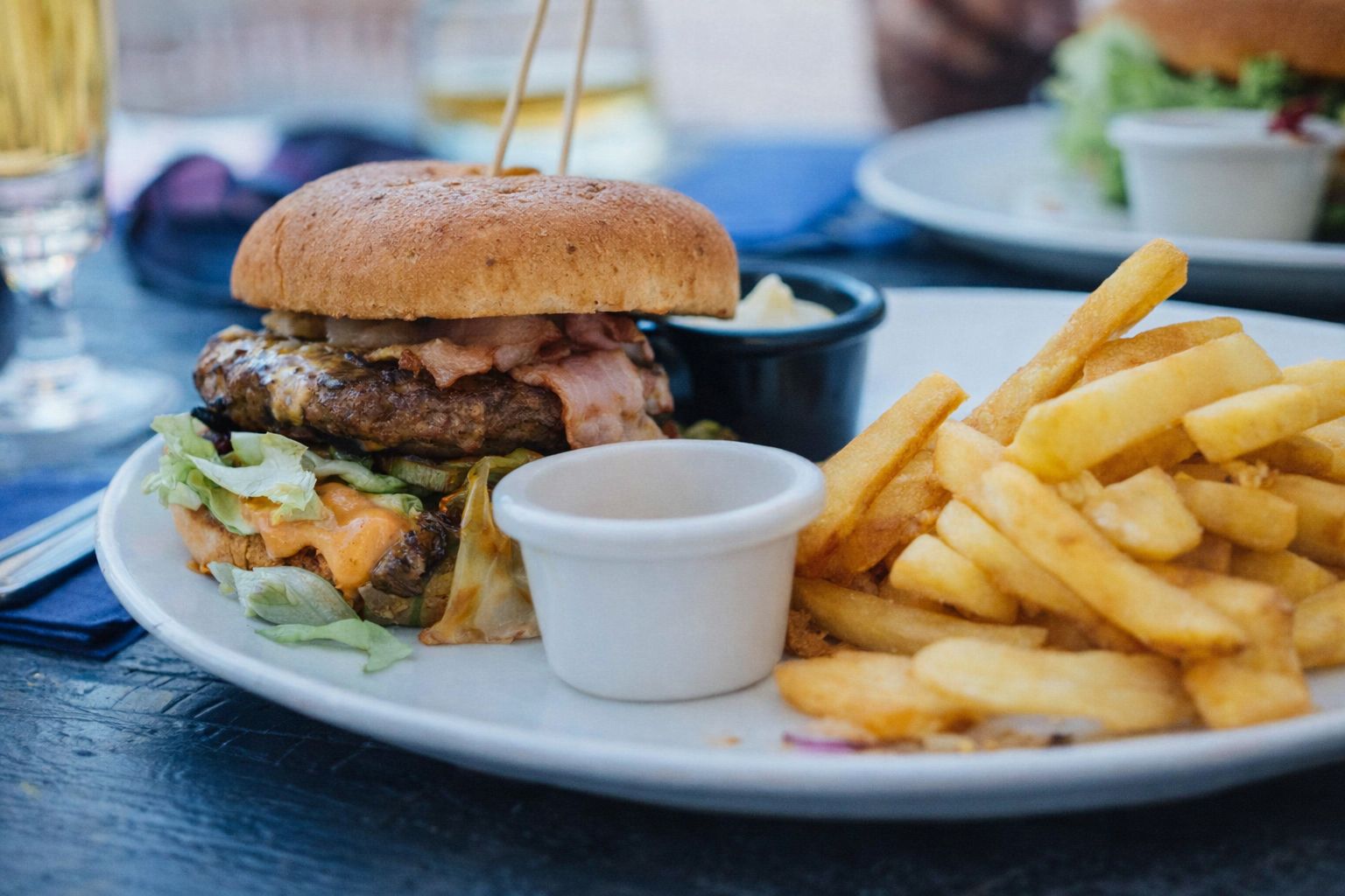 En saftig hamburgare med pommes frites serverad på en vit tallrik utomhus.
